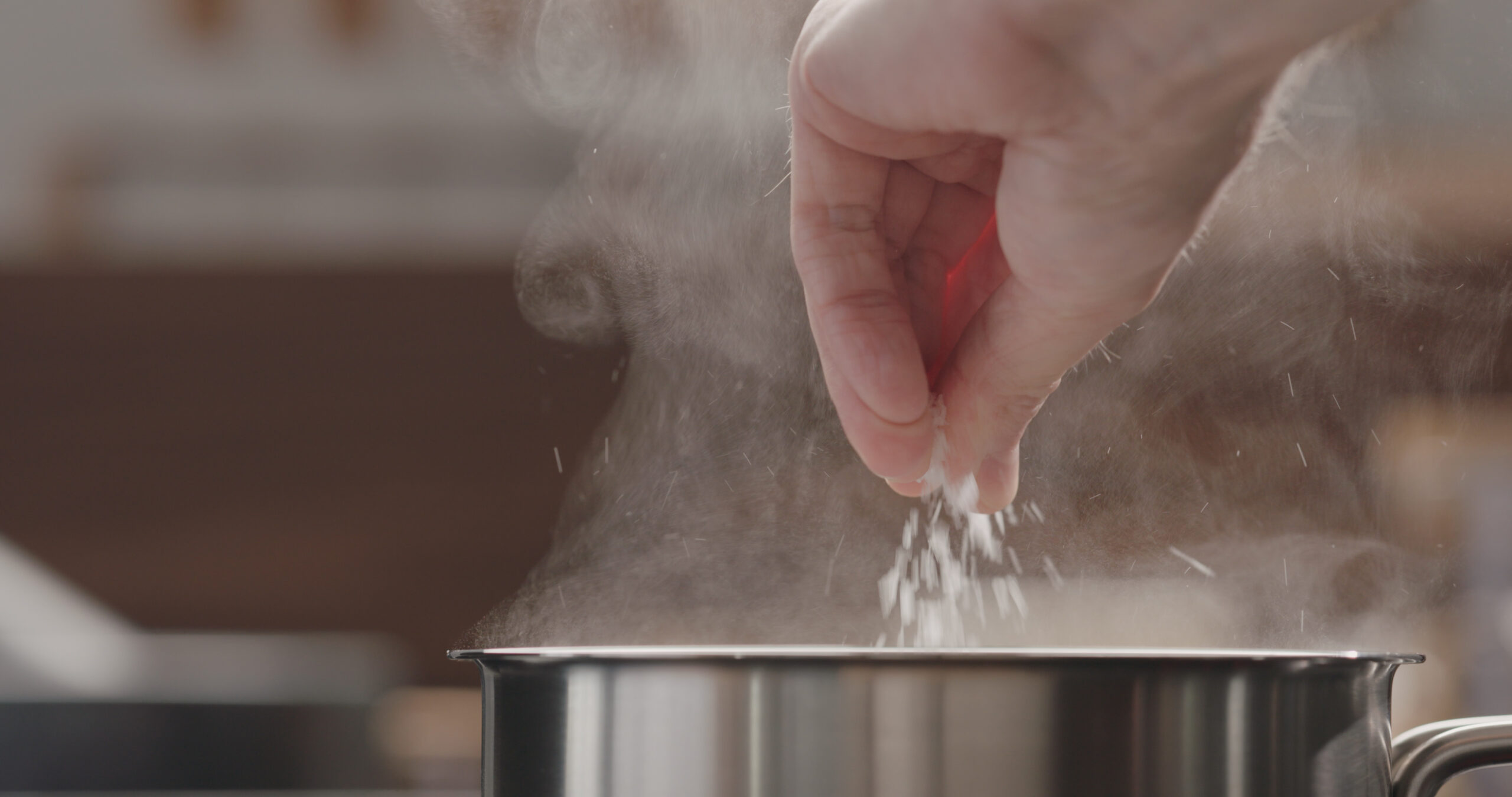 man adding salt to boiling water in saucepan